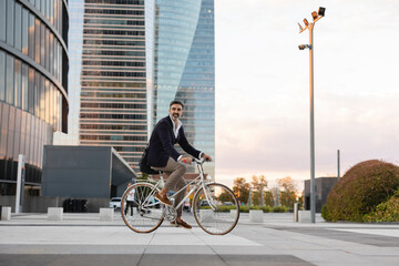 Mature commuter riding bicycle in front of office building at sunset