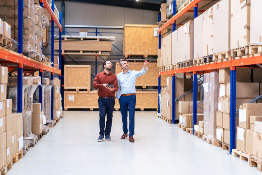 Businessman with colleague pointing at containers in warehouse