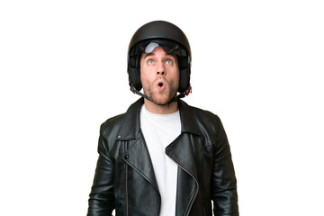 Young caucasian man with a motorcycle helmet isolated on green chroma background looking up and with surprised expression