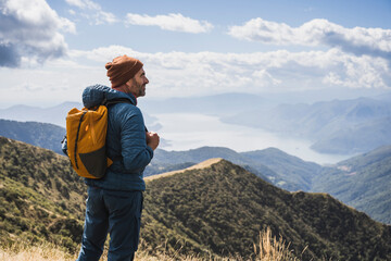 Mature man wearing knit hat standing with backpack in front of mountains