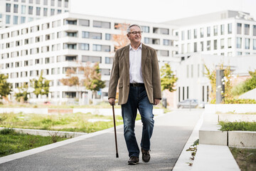 Senior man with cane walking on footpath
