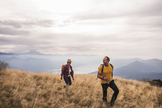 Happy Mature Couple Hiking On Mountain Under Cloudy Sky