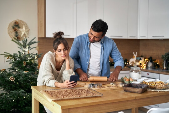 Multi Ethnicity Couple Baking Christmas Cookies And Looking At Mobile Phone