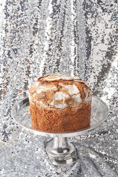 Freshly baked panettone cake on cakestand against shiny silver sequins