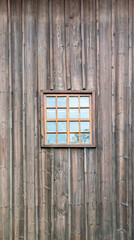 A small window with muntins against the background of a wall covered with wooden boards in a vertical arrangement.