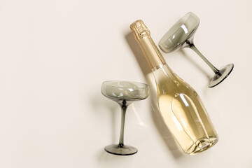 Champagne or sparkling wine bottle, champagne glasses from tinted grey glass on beige background. Festive drink minimal concept. Modern wine glasses, dark colored glass. Creative top view, flat lay