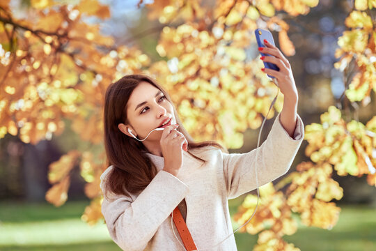 A young beautiful woman walks in the autumn park and talks on the phone. A girl with a smartphone takes photos in an autumn forest