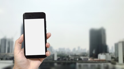 Mock up image of hand holding black smartphone with blank white screen on blurred city background. Concept for display your design.