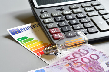 Close up of energy saving light bulb, calculator and energy efficiency rating table with 500 euro...
