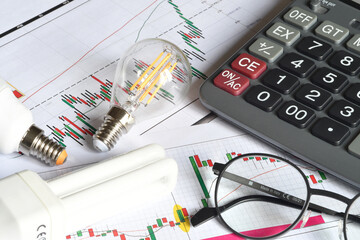 Close up of energy saving light bulbs, calculator and glasses on printed graph. Concept for the...