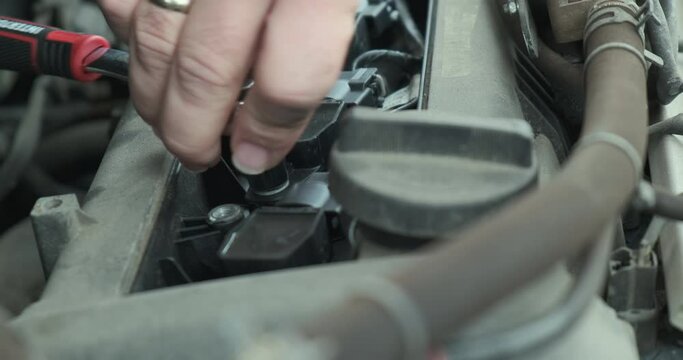 Auto mechanic unscrews the bolts near the engine of the car. Close-up, changing spark plugs in a car.