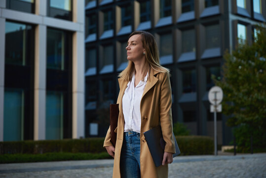 Millennial Business Woman Wearing Coat Walking At City Street With Laptop At Summer Day.