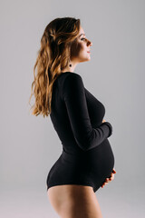 Beautiful pregnant woman wearing casual clothes and smiling against a white background. Attractive pregnant woman touching her round belly and feeling happy