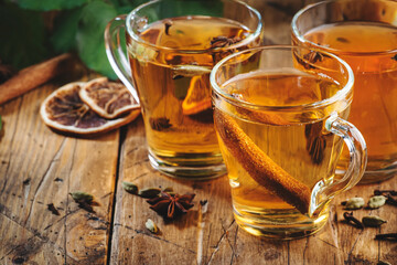 Mulled Cider glass cups: apple, pear and orange flavored  hot cider with spices. Fermented low alcohol cocktail fruit drink on ustic wooden table. Background with leaves