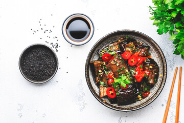 Gegrilde pittige aubergine met hete rode chilipepers, sojasaus, knoflook en sesamzaadjes in aziatische stijl, witte tafelachtergrond, bovenaanzicht
