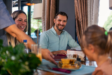 The waiter in the restaurant brings lunch to the whole family of three. Family launch concept.