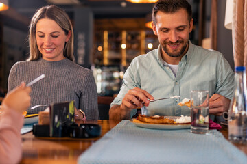 young married couple enjoys a fun lunch time with their little daughter in the restaurant.