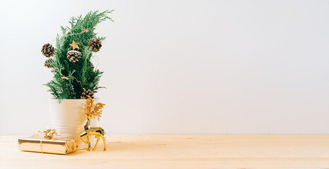 Creative natural miniature Christmas tree in pot on wooden table with gift boxes and white background. Xmas greeting card with copy space. Happy New Year