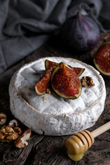 White round goat homemade camembert cheese with figs on top and honey. Wooden table background. Dark closeup styling food. Top view.