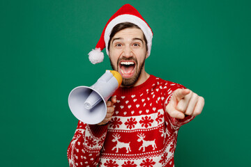 Merry young man wear red warm knitted sweater Santa hat posing hold scream in megaphone announces...