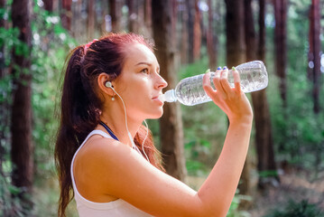 Young woman drinking water after jogging at summer,spring park,forest.