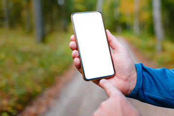 Blank space mockup.Hiker man standing on a trail autumn forest and showing of smartphone white screen.Technology in nature concept.Selective focus.