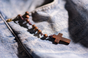 wooden brown cross with rosary crown on jeans color background