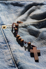 wooden brown cross with rosary crown on jeans color background