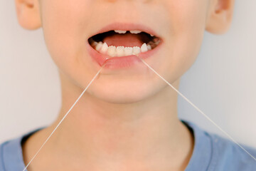 funny little boy flossing his teeth. soft thread of floss silk or similar material used to clean...
