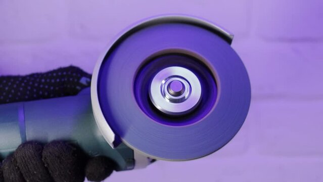 Soft start of the angle grinder in the worker's hand, close-up. Slow motion