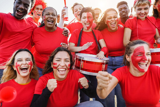 Multiracial red sport fans screaming while supporting their team - Football supporters having fun at competition event - Focus on center girl face