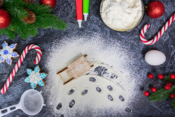 spilled flour with traces of toy sleigh on black textured table with christmas tree, red christmas...
