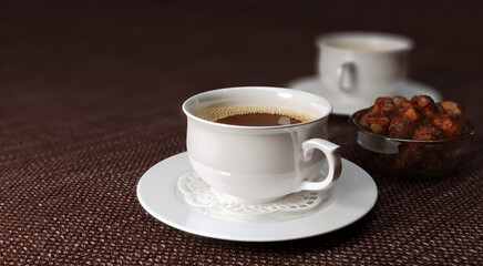 Two white cups of coffee on brown table.