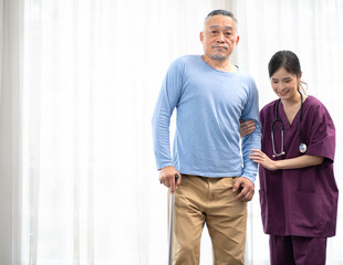 Beautiful nurse helps senior man patient in hospital holding stick walking. Old man has illness recovery and walks using stick with female doctor's support at nursing home. Elderly rehabilitation.