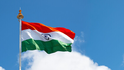 Large Indian flag or flag of India waving in front of blue sky during sunny day, space for text