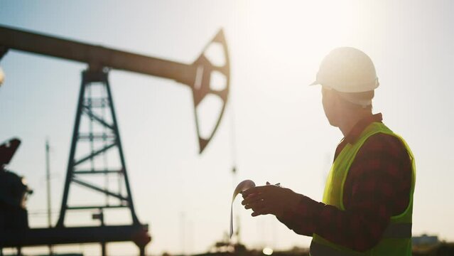 oil industry. engineer next to an oil rig signs a paper contract. oil production business finance concept. gas production. a worker oil production next an station. sun a worker in hard hat works