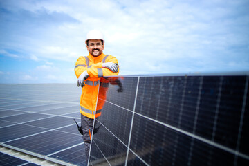 Portrait of worker expert standing on the roof leaning against solar panel and smiling.
