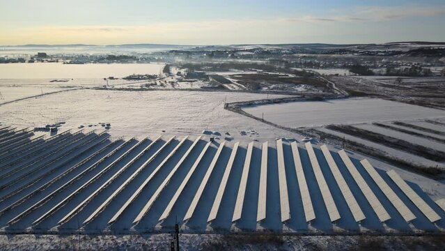 Aerial view of snow covered sustainable electric power plant with many rows of solar photovoltaic panels for producing clean electrical energy. Low effectivity of renewable electricity in winter