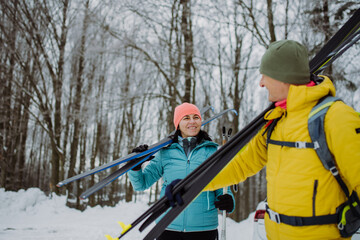 Fototapeta na wymiar Senior couple crossing forest with skis in hands.