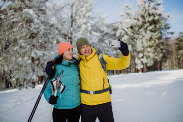 Senior couple taking selfie during cross country skiing in snowy forest.