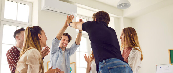 Team of school students achieving goal together. Group of happy cheerful joyful friends smiling and high fiving each other in classroom. Teamwork, education, success, fun concept. Banner background