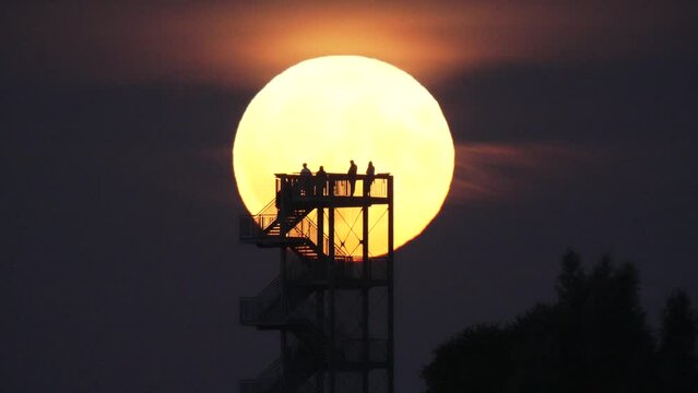 Mesmerizing rising supermoon with a silhouette of a tower with people