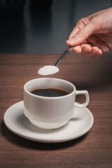 Adding sugar to a cup of black coffee
