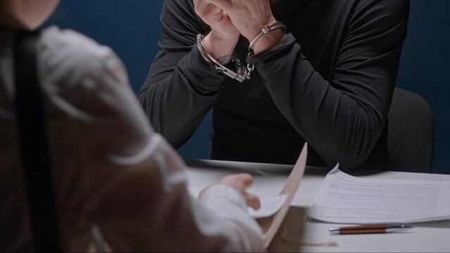 Female detective cop shouts and forces russian mafia to sign documents papers. Interrogation of criminal in handcuffs. Police officer with evidence folder. FBI agent and detained guy