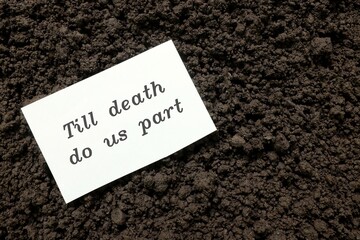 Till death do us part wedding vow concept. Handwritten note on paper on grave soil.