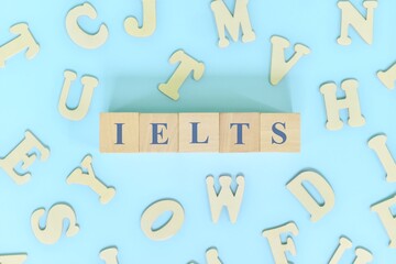 IELTS or international english language testing system exam or test concept. Wooden blocks typography flat lay on blue background.