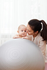 mother playing with her baby girl on a fitness ball
