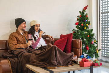 European couple looking out the window in winter clothing holding glasses of red wine sitting on...