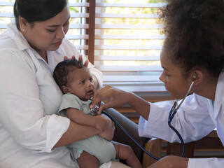 Cute little baby boy in mother's arms, looking at the pediatrician. Doctor using stethoscope listening for the heartbeat of the little one.