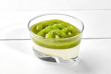 Coconut panna cotta with kiwi and mint coulis in glass on white wooden background